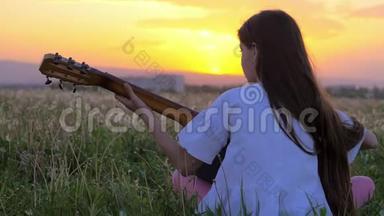 美丽的日落小女孩背着相机坐在蒲公英的田野里弹吉他。 远离户外