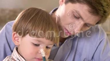 年轻的<strong>父亲和</strong>他的小<strong>儿子在</strong>纸上画画，拿着平板电脑，爸爸帮助<strong>和</strong>教他的<strong>儿子</strong>如何写作