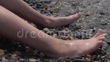 一个孩子的腿`特写被波浪淹没了。 卵石沙滩喧闹的海浪拍打着孩子们`双腿