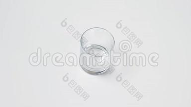 女人`手把一个透明的空玻璃放在白色的桌子上，往里面倒纯净水，然后把拿下来