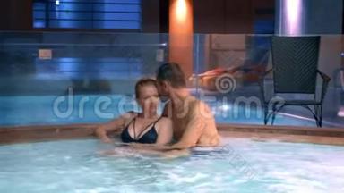 情侣们在室外热水浴缸中放松。 快乐的年轻女人和男人在游泳池附近的热水中放松。