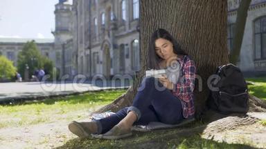 亚洲女孩坐在树下，在笔记本上写得很快，灵感，诗歌