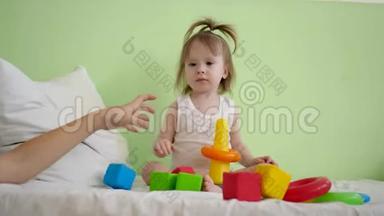 孩子们在床上玩立方体，和妈妈一起建塔。 孩子和妈妈在床上玩彩色方块
