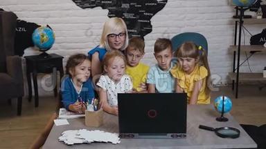 快乐的老师在地理教室里和学生们一起使用笔记本电脑。帮助高加索儿童学习的老师