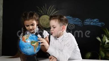学校观念。 小学生们坐在书桌前玩地球仪。 孩子们选择度假旅游的地方