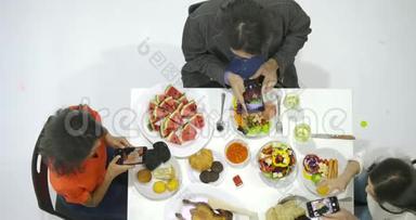 一群朋友在<strong>晚宴</strong>上和桌子上的所有人一起使用他们的智能手机拍摄晚餐食物的照片。