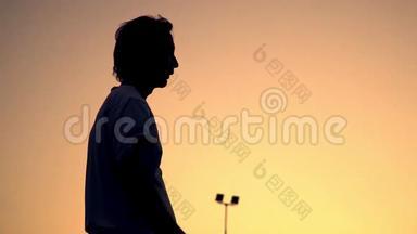 打大网球。 运动员站在橙色日落的背景上，拿着球拍，然后把球拍放在肩上