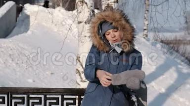 穿着蓝色<strong>羽绒服</strong>的女人，带着毛皮罩，在冬季公园打电话给她的手机，戴上手套。