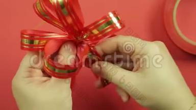 女人`双手伸直粉红色丝带礼物蝴蝶结的花瓣，给它蝴蝶结的形状。 红色背景