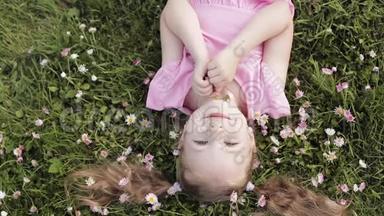 特写微笑的小可爱小女孩躺在绿草上捧着鲜花看着镜头