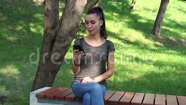 年轻漂亮的<strong>女孩</strong>坐在公园的长凳上，在手机里浏览<strong>社交网络</strong>磁带。