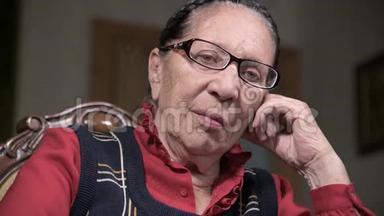 一个戴着眼镜的老年沉思的女人在室内坐着思考，靠在手臂上的肖像。 老年妇女80岁