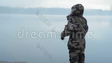 穿着<strong>迷彩服</strong>的女渔夫在一个初秋的早晨，在雾中向河上扔了一根鱼竿