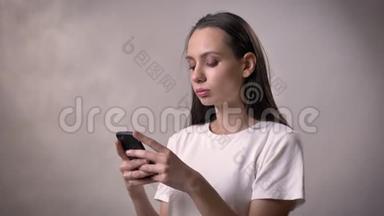 年轻严肃的黑发女孩正在智能手机上输入信息，交流概念，灰色背景