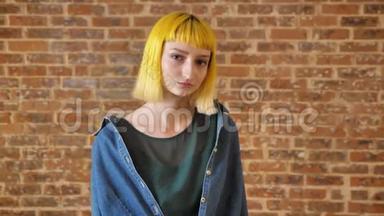 年轻漂亮的女人，一头<strong>黄发</strong>，看着摄像机，站在砖墙的背景附近，不寻常的人