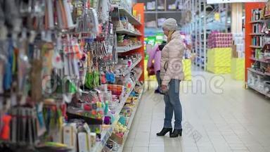 一个戴着帽子和<strong>羽绒服</strong>的女人穿过超市。 她看着货架上的货物，选择