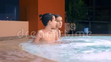 幸福的家庭在户外按摩浴缸放松。 两个儿童青少年在游泳池附近的热水中放松。