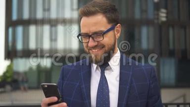 英俊的商人留着胡子，戴着眼镜，微笑着看着商业区的智能手机屏幕。