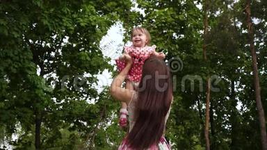 小女孩和妈妈穿着优雅的衣服在温暖的绿色公园里玩耍。 快乐的妈妈和宝宝在城里散步