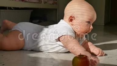 六个月大的婴儿躺在地板上，伸手要一个红苹果。 孩子<strong>学会</strong>了爬行