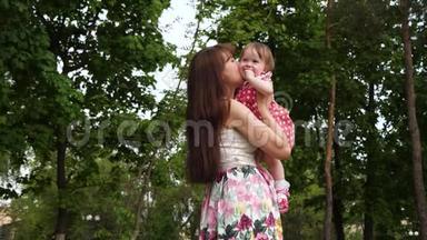 <strong>妈妈</strong>把婴儿抱在<strong>怀里</strong>，亲吻他的脸颊。 女孩在绿色公园和她的父母笑。 慢动作。