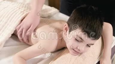 特写男理疗师按摩师为躺在按摩床上的小男孩做一个疗愈放松的按摩。 回去