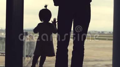 父女两人<strong>望</strong>着<strong>窗外</strong>，看着机场区域。 在远处可以看到飞机。