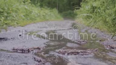 草地背景下雨中泥泞小路的特写。 库存录像。 在泥泞中拍摄雨滴的宏观拍摄