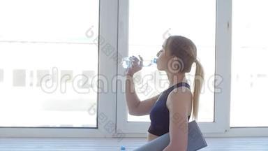 健身理念。 年轻女子在白色室内运动后饮用水