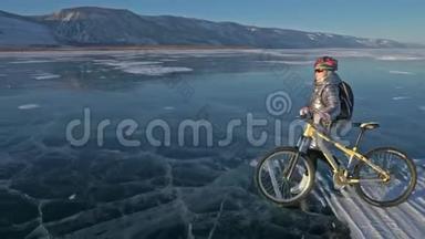 女人在冰上骑自行车。 女孩穿着银色的<strong>羽绒服</strong>，背包和头盔。 骑自行车的人