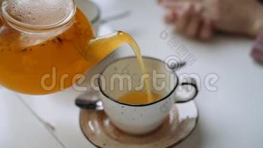 橙色的沙棘茶在茶壶里倒入一个杯子上，用女人的手。