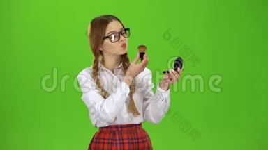 戴眼镜的女学生用刷子把鼻子涂成粉末. 绿色屏幕