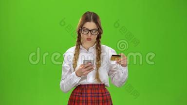 戴眼镜的女孩用金卡在电话上拨号码。 绿色屏幕