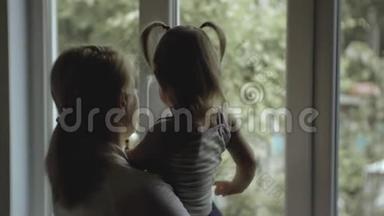 母亲站在一扇窗前，一个小孩子站在一个剪影里