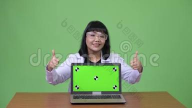 美丽的亚洲女医生戴着<strong>防</strong>护<strong>眼镜</strong>，手提电脑，竖起大拇指