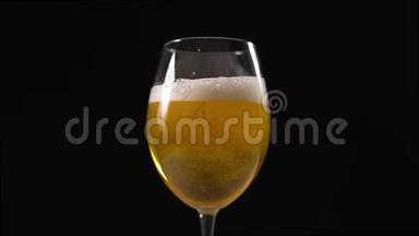 金色泡沫啤酒缓慢地倒入玻璃杯中，黑色背景下的啤酒杯，啤酒中的气泡，淡啤酒