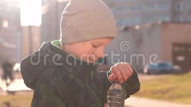 男孩从街上的瓶子里喝水。 打开瓶子，喝水，关闭瓶子。