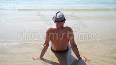 夏季生活方式高清视频美丽的年轻晒黑男子戴帽子。 享受生活，坐在海滩上，旅行的时间