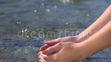 女子双手抓举清澈见底的淡水在户外的山河中，滴入水面