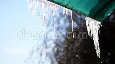 冬天，霜冻，下雪，晴天。 特写，大的透明冰柱挂在屋顶上，对着天空。