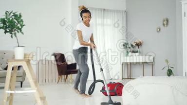 开朗的家庭主妇在家里打扫卫生时使用<strong>吸尘器</strong>，通过耳机听音乐，跳舞和