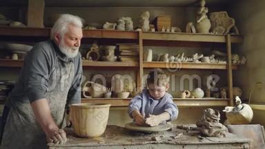 小男孩正在爷爷的工作室里`泥塑制品，而他关心的老爷爷正站在他身边