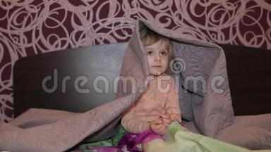 快乐的小女孩躲在毯子下面看电视。 <strong>儿童睡眠</strong>概念