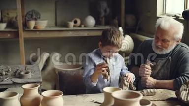 可爱的男孩在爷爷的陶艺工作室玩泥巴，而老人在揉泥巴
