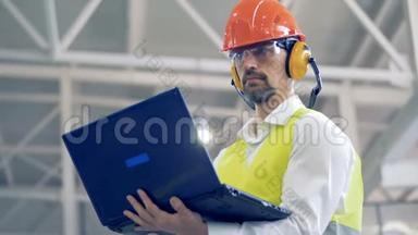 这位工厂的男员工正在用他的笔记本电脑工作，环顾四周