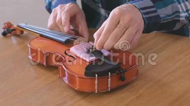 一个穿着格子衬衫的年轻人<strong>正在修理</strong>坐在桌子旁的小提琴。调整字符串的声音