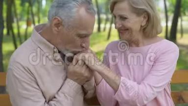 幸福的老夫妻在公园拥抱，男人亲吻妻子的手，爱到老