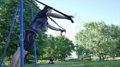 男人开始在一个夏季公园里的健身圈上做俯卧撑。 从下面的镜头4K慢镜头