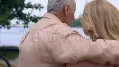 老人抱着女人在公园河边的花园里放松，幸福的老年夫妇