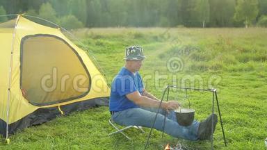 一个人靠近火边的帐篷，看着一个<strong>沸腾</strong>的<strong>锅</strong>。